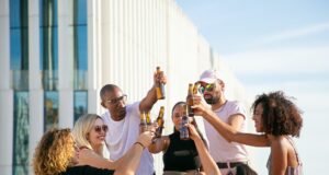 joyful diverse friends clinking beer bottles on rooftop
