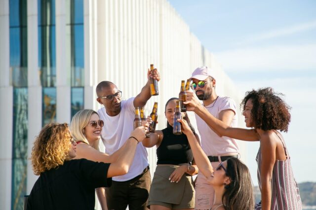 joyful diverse friends clinking beer bottles on rooftop