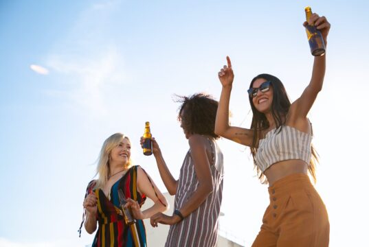 delighted friends having drinks and dancing on sunny terrace