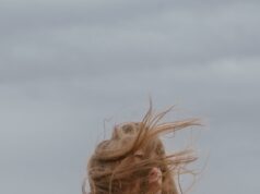 dreamy young woman with windy hair recreating on seashore against cloudy sky