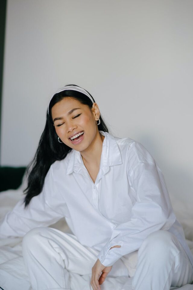 positive young ethnic woman smiling with closed eyes on bed